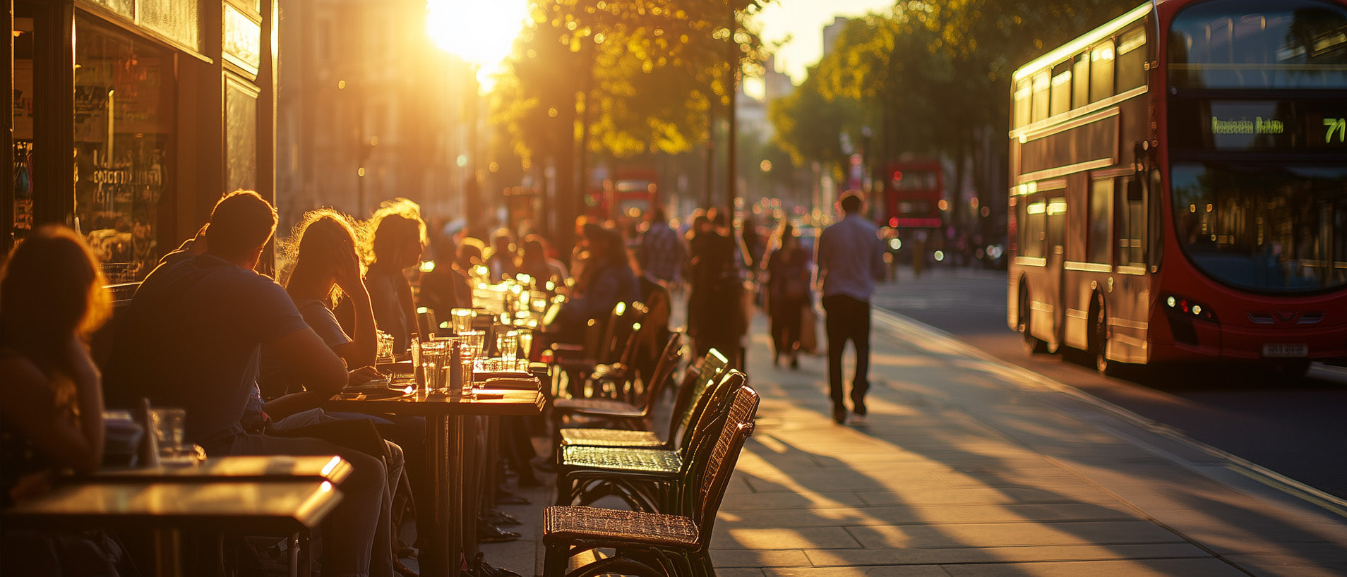 People sit at cafe tables at sunset on a busy London street